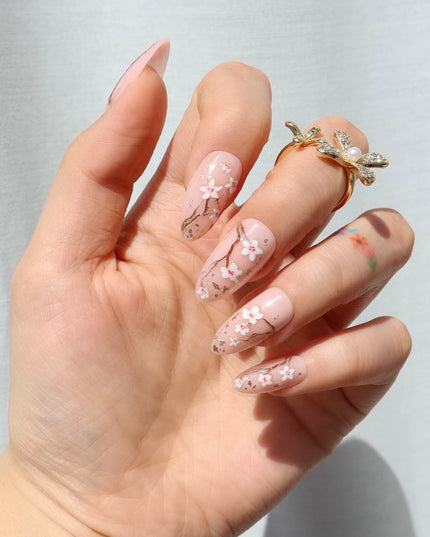 As effortless as cherry blossoms drifting in the wind. Soft Sakura press-ons embrace the beauty of simplicity with delicate floral accents on a soft nude base. Wispy branches stretch across each nail, adorned with hand-painted cherry blossoms and subtle gold flecks for a natural glow.